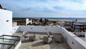 Eine Dachterrasse mit Sitzgelegenheiten im Freien und Blick auf den Strand.
