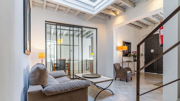 Ein modernes Wohnzimmer mit einer Couch, einem Couchtisch und einem Korbstuhl. Eine Treppe führt in einen weiteren Bereich.