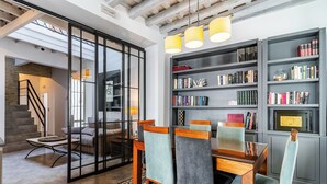 Ein modernes Wohnzimmer mit Essbereich, ausgestattet mit einer Treppe, Bücherregalen und einem großen Fenster.