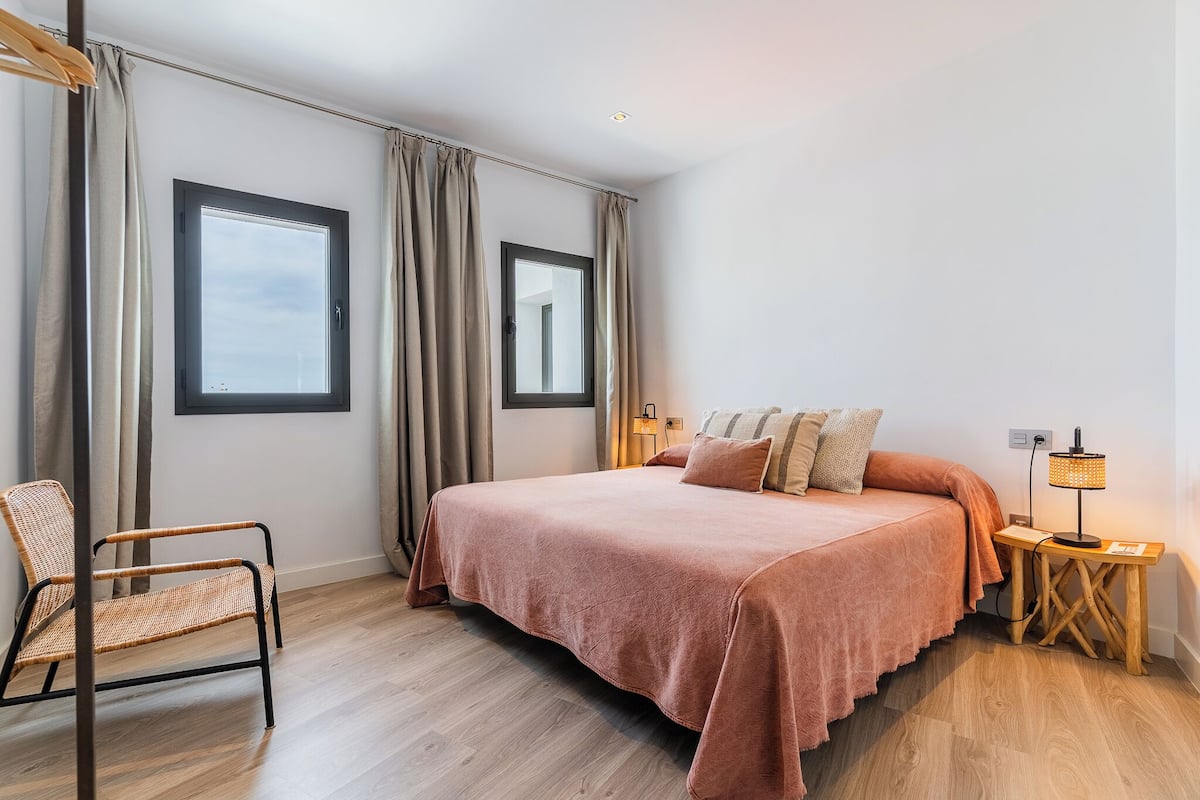 A bedroom with a bed, a chair, a nightstand, and a window.