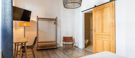 A bedroom with a bed, a desk with a chair, a hanging light fixture, a wooden wardrobe, and a sliding door.