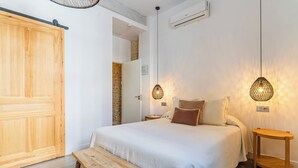 Ein Schlafzimmer mit großem Holzschrank, einer Bank, einem Bett mit weißer Bettwäsche, zwei Nachttischlampen und einem kleinen Nachttisch.