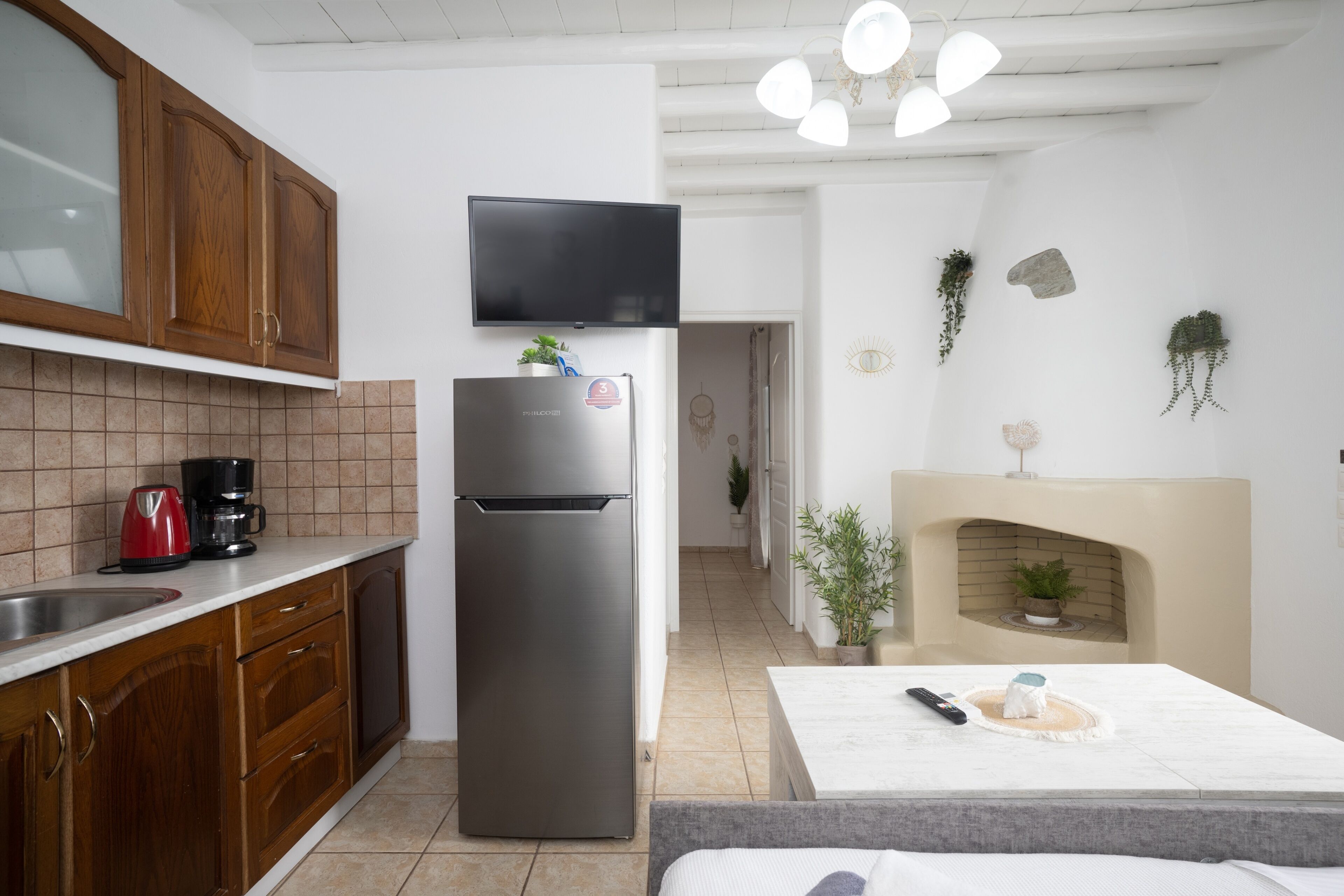 A modern kitchen with wooden cabinets, a stainless steel refrigerator, a flat-screen TV, and a fireplace.