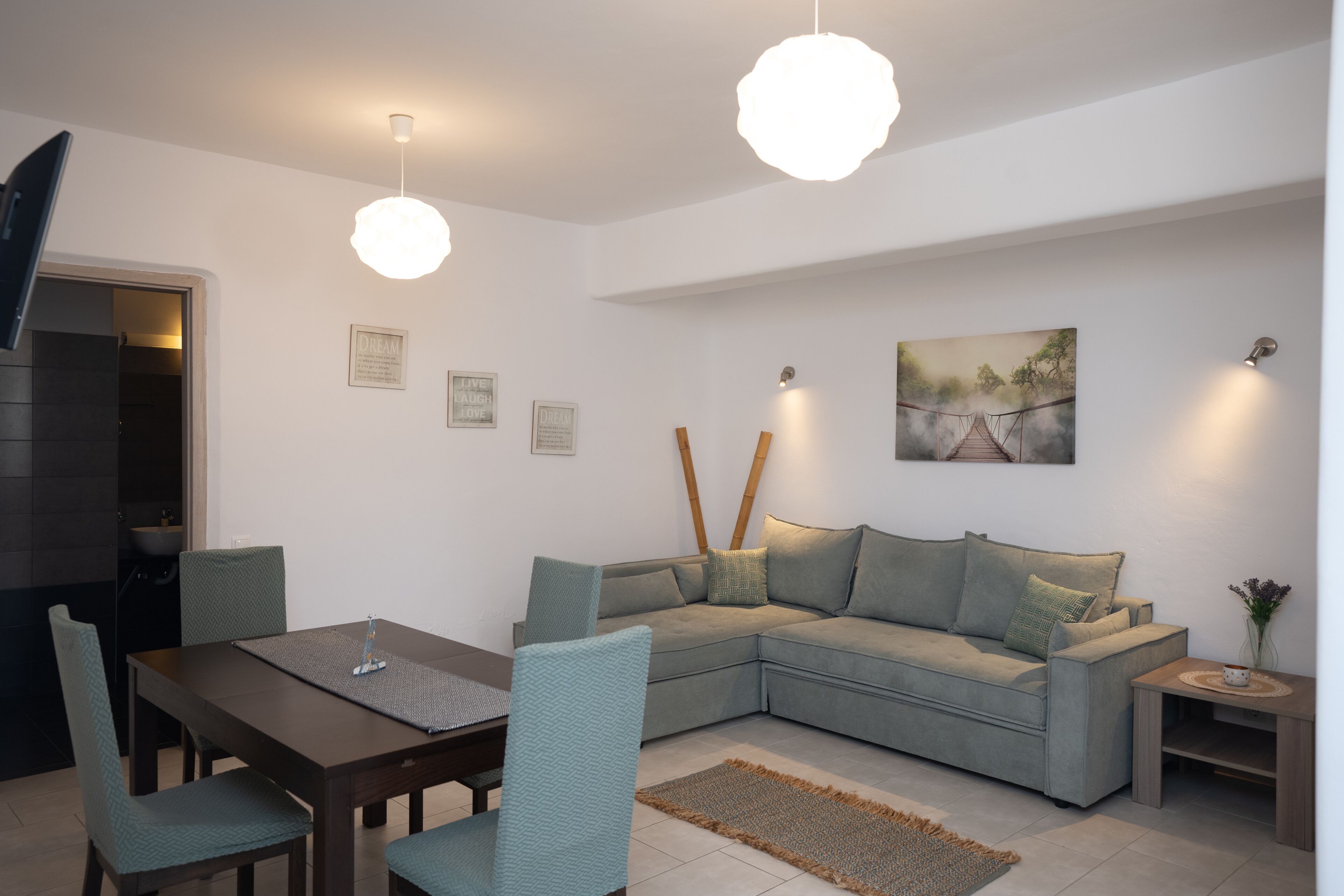 Un salon moderne avec un canapé d’angle, une table à manger et deux lampes suspendues.