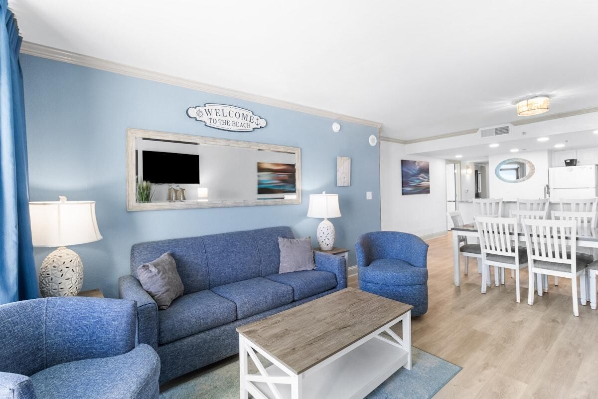 A living room with a blue sofa, a wooden coffee table, and a dining area with white chairs and a table.