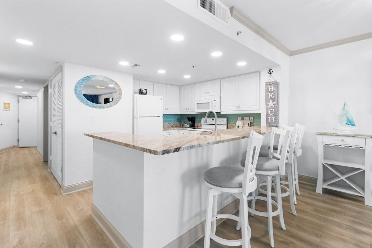 A modern kitchen with white cabinets, a marble countertop, and a central island with bar stools.