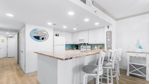 A modern kitchen with white cabinets, a marble countertop, and a central island with bar stools. - Coastal Getaway 4th Flr 3BR Angle Ocean View Condo (Myrtle Beach)