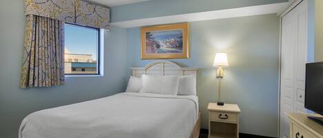 Une chambre d’hôtel avec un lit, une table de chevet avec une lampe, une commode, un téléviseur et un tableau au mur.
