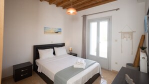 Un dormitorio con techo de madera, una cama con ropa blanca, una mesita de noche, una lámpara de noche y una ventana con cortinas.