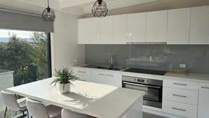 Een moderne keuken met witte kasten, een centraal eiland met stoelen, een inbouwoven en hanglampen.