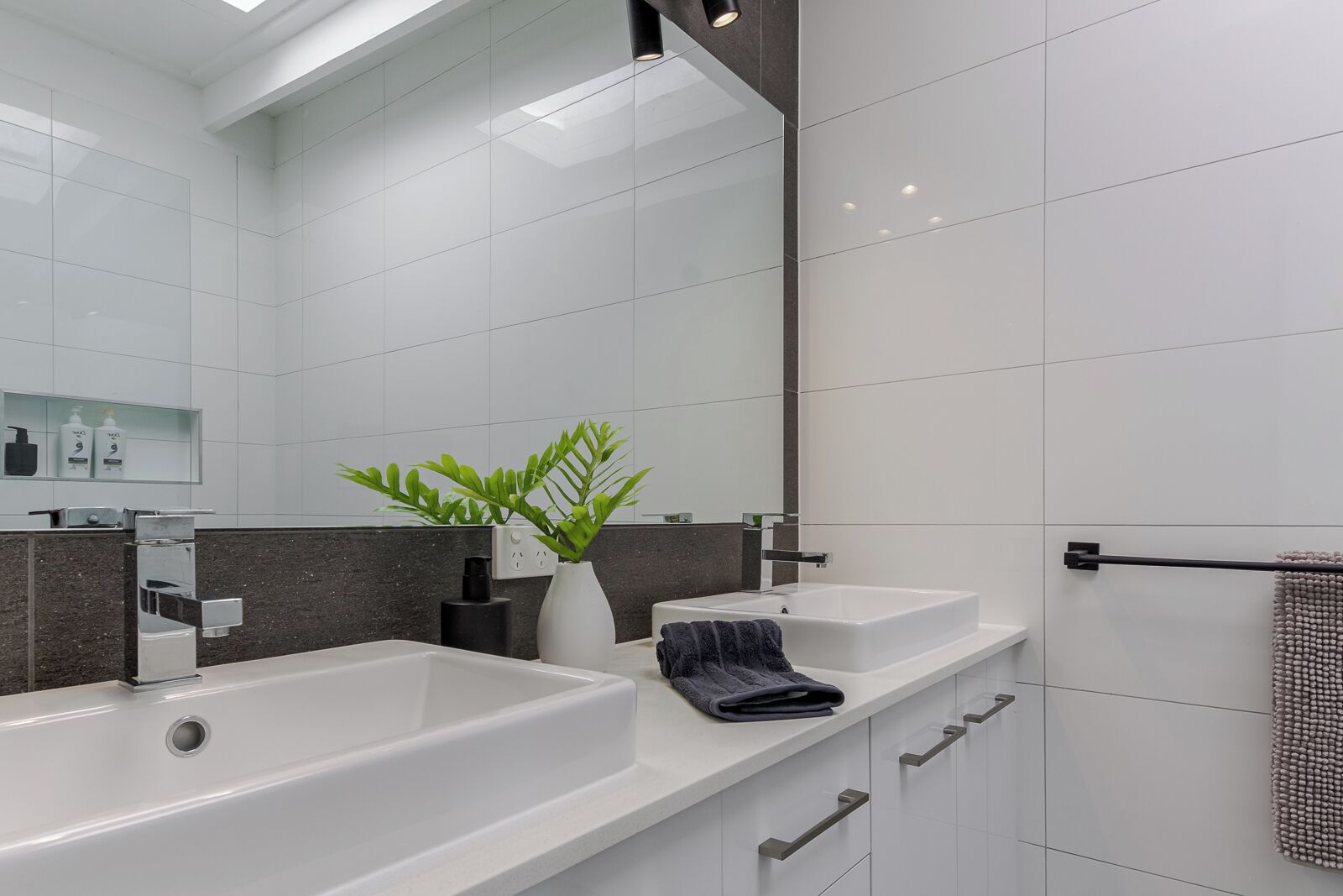 Une salle de bain moderne avec deux vasques, un grand miroir, une plante et un porte-serviettes.