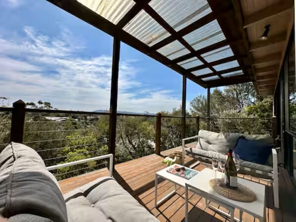 Um deck externo com piso de madeira, uma mesa branca e um sofá.