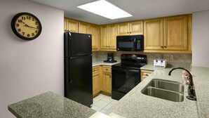 A kitchen with wooden cabinets, a black refrigerator, a microwave, a stove, and a sink.