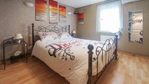 Ein Schlafzimmer mit Bett, Nachttisch, Lampe, einem Fenster mit Vorhängen und Wandbildern.