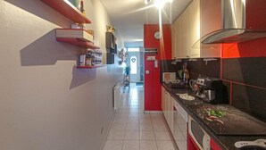Eine schmale Küche mit rot- und schwarz gefliesten Wänden, einer Kaffeemaschine und einem Spülbecken.