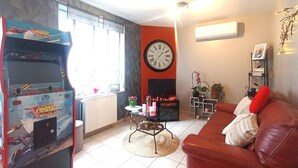 Ein Wohnzimmer mit einem roten Sofa, einer Uhr, einem Kamin und einer Spielkonsole.