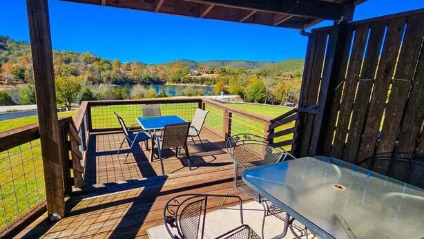 A covered outdoor area with a table and chairs, a grill, and a view of a lake and hills. - Great location for exploring Northwest Arkansas! (Holiday Island)
