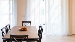 Un coin repas avec une table et des chaises en bois, une assiette de nourriture et des rideaux légers.
