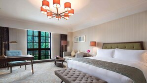 Ein Hotelzimmer mit einem großen Bett, einer Sitzecke mit einer Couch und einem Tisch, einer Bank und einem großen Fenster mit Blick auf Bäume.