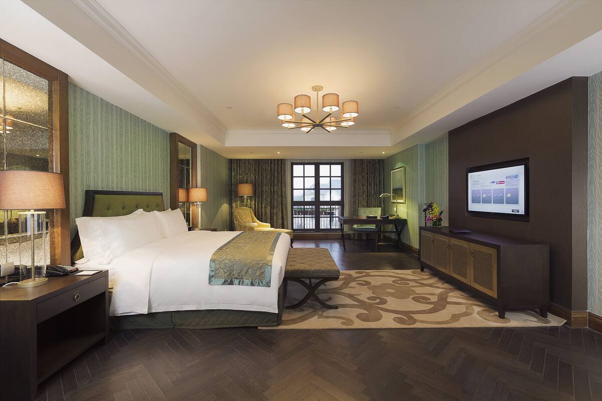 Een hotelkamer met een groot bed, een bureau, een televisie en uitzicht op de omgeving.