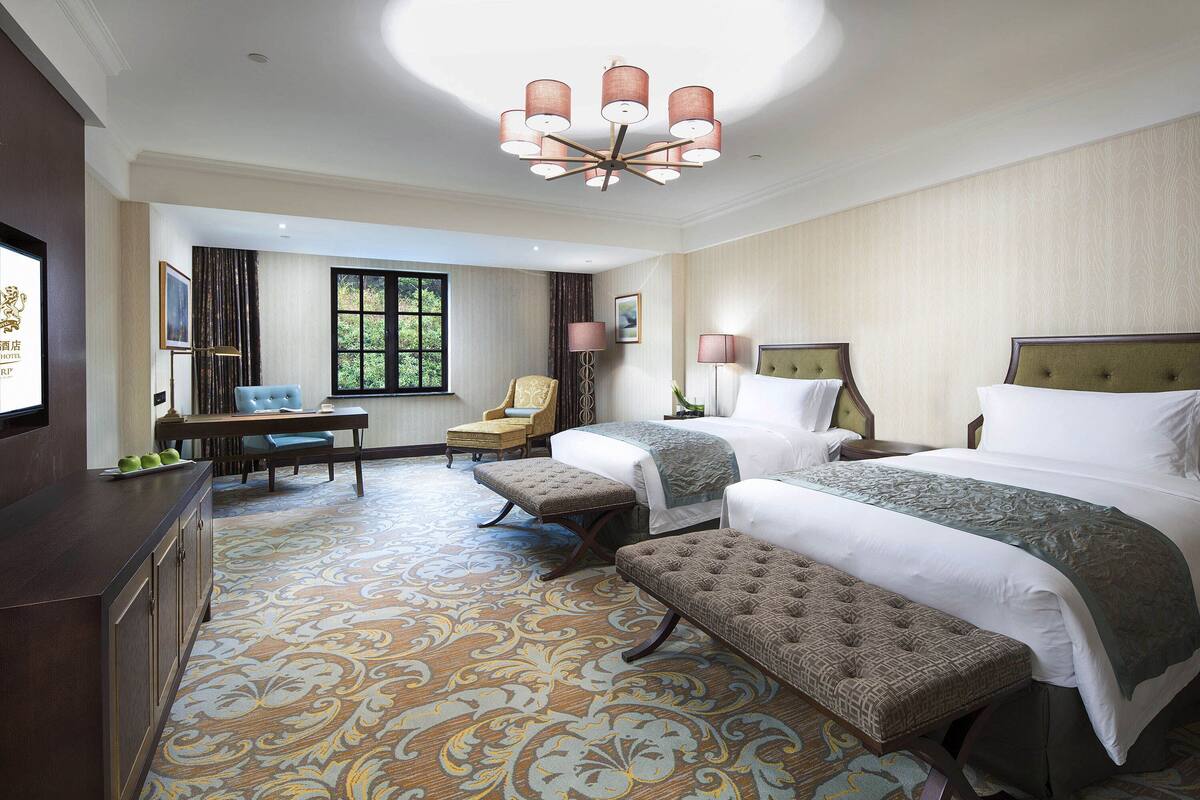 Een hotelkamer met twee bedden, een zithoek met een tafel en stoelen, en een groot raam.