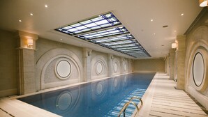 Ein großes Hallenbad mit einer Dachfensterdecke, umgeben von Wänden mit kreisförmigen Zierelementen und einem gefliesten Boden.
