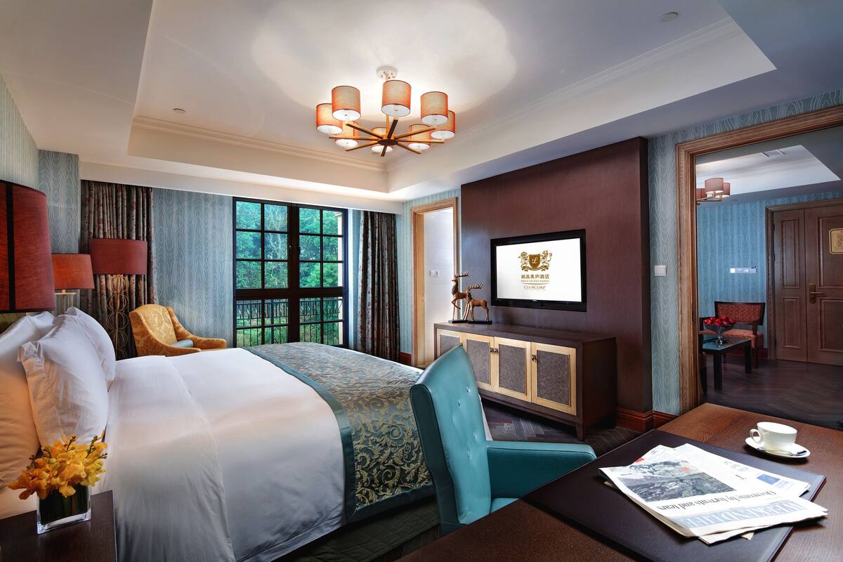 Hotelkamer met een groot bed, een televisie, een bureau met een krant en uitzicht op het buiten.