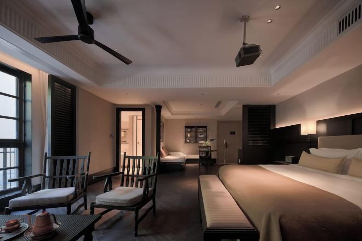 Une pièce spacieuse comprenant un lit, un canapé, une table à manger et des chaises. On y trouve également un ventilateur de plafond et un téléviseur fixé au mur.