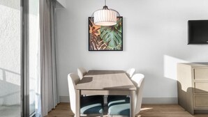Een eethoek met een houten tafel en stoelen, een hanglamp, een ingelijste afbeelding, een televisie en een glazen schuifdeur.