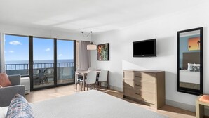 Een moderne hotelkamer met een groot bed, een bureau en een televisie. Er is een balkon met uitzicht op zee.