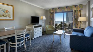 Ein Hotelzimmer mit Esstisch, Stühlen, Fernseher, einer Couch und einem Balkon mit Blick.