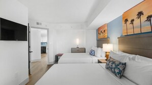 A hotel room with two beds, a flat-screen TV mounted on the wall, a painting of palm trees, and a nightstand with a lamp. - 12th Floor Beachfront Getaway in Two Bedroom Bliss (Myrtle Beach)