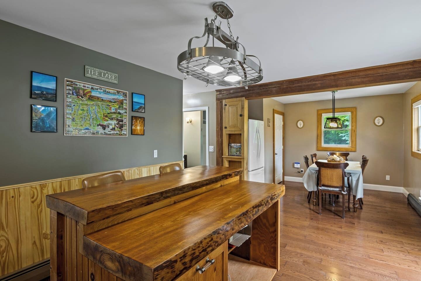 Un grand espace dédié à la salle à manger, avec une longue table en bois et des chaises, une cuisine équipée d’un réfrigérateur, et une table à manger dressée pour quatre personnes.