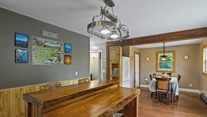 Un grand espace dédié à la salle à manger, avec une longue table en bois et des chaises, une cuisine équipée d’un réfrigérateur, et une table à manger dressée pour quatre personnes.