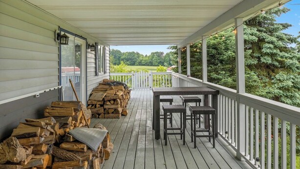 Une véranda couverte avec une terrasse en bois, une pile de bois de chauffage et du mobilier d’extérieur.