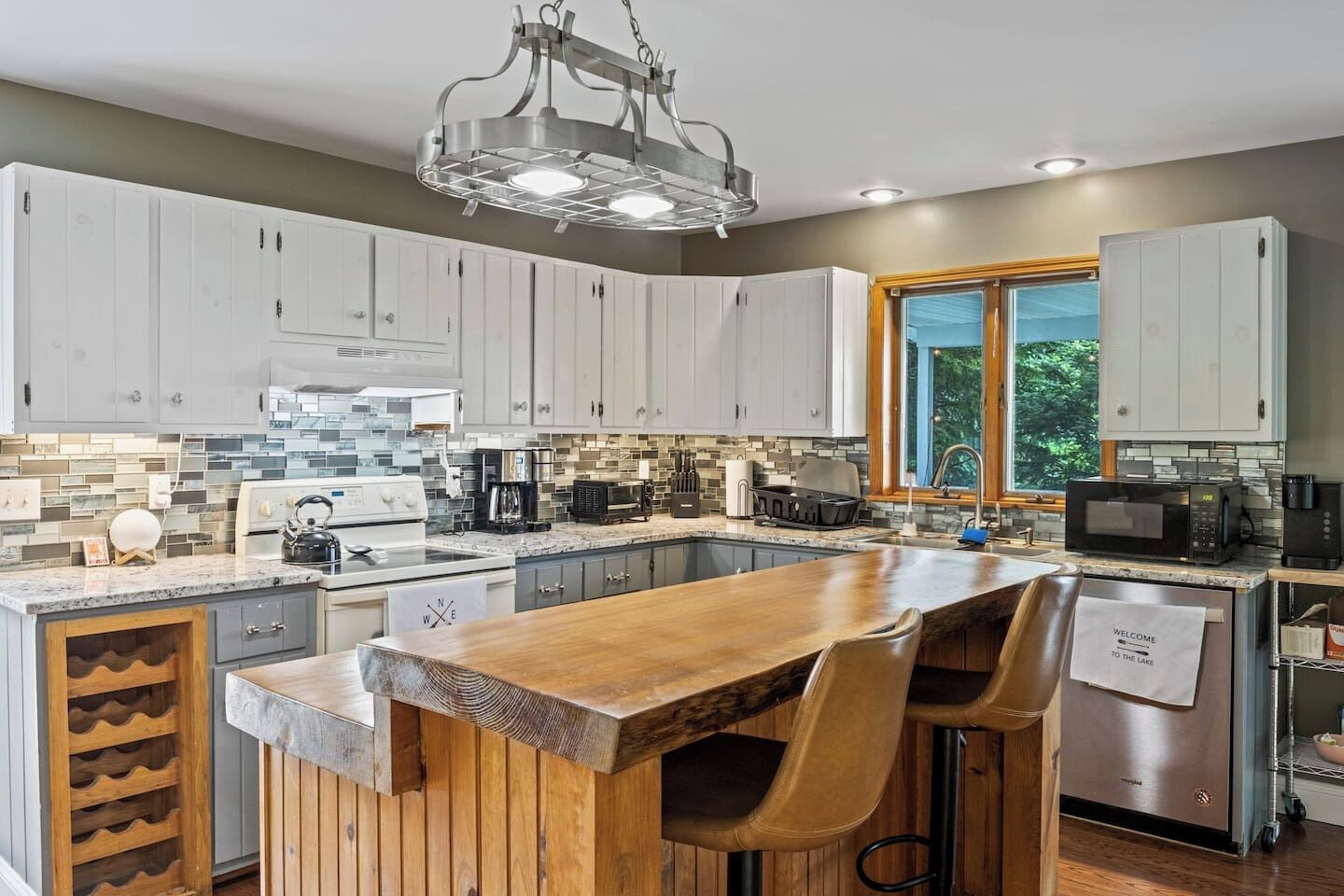 Une cuisine moderne avec des meubles blancs, un îlot central en bois et une grande fenêtre.