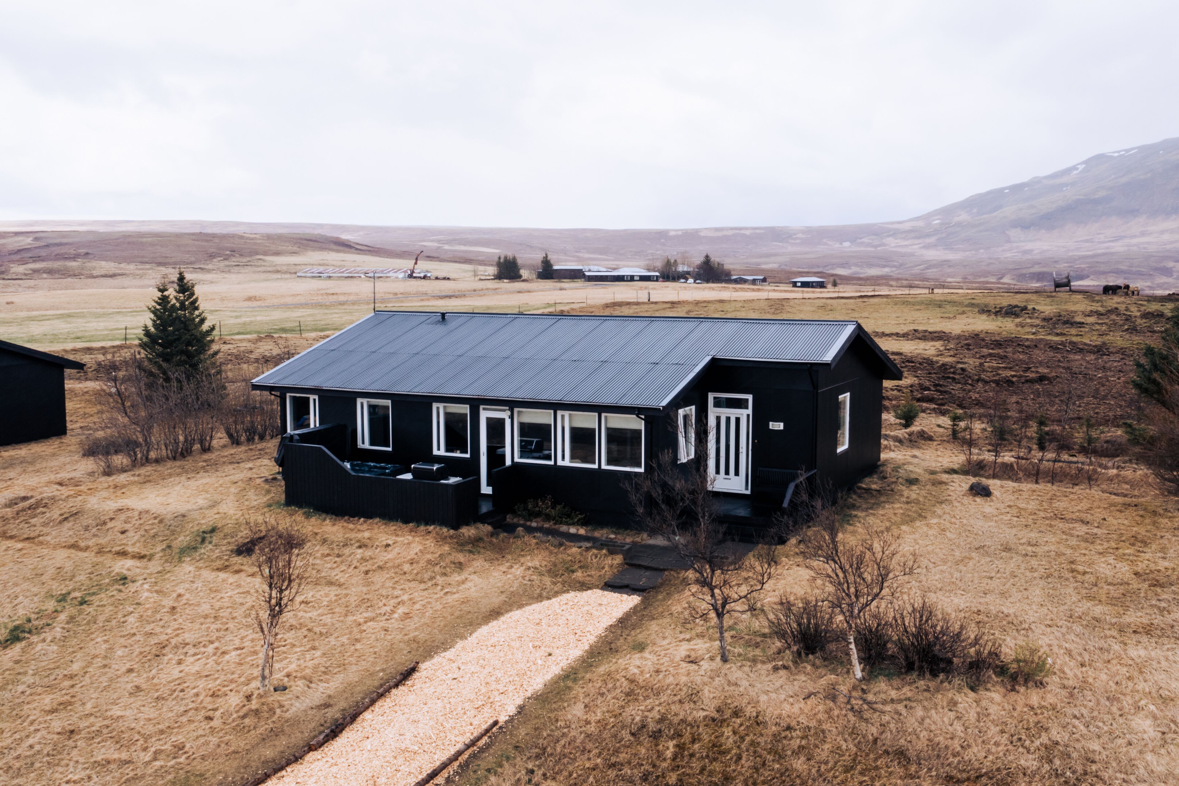 A black house with a sloped roof and white trim, surrounded by a dry, grassy landscape with distant hills.