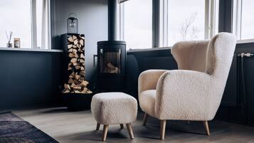 A modern living room with a large window, a fireplace, a fluffy armchair, and a matching ottoman.