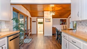 A modern kitchen with wooden flooring, white cabinetry, and a central island. - Honeoye Cottage | 50' Lakefront | Dock | FLX (Honeoye)