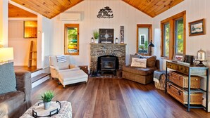 A cozy cabin interior with a stone fireplace, wooden ceiling, and a comfortable seating area. - Honeoye Cottage | 50' Lakefront | Dock | FLX (Honeoye)