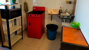 Una cocina compacta con estufa roja, un fregadero, un microondas y un cubo de basura.