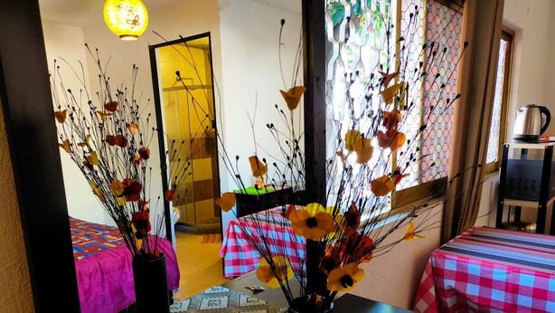 Una habitación con cama, una mesa con un jarrón de flores, un espejo que refleja la habitación y una ventana con vistas al exterior.