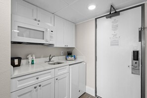 A kitchenette with white cabinets, a microwave, a sink, and a coffee maker. - Experience Serenity Oceanfront Suite 4th Floor (Myrtle Beach)