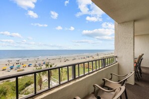 A balcony with a view of a beach, chairs, and a railing.