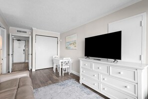 A modern living room with a flat-screen TV, white furniture, and a door leading to another room.