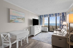 Una habitación con un escritorio blanco, una televisión, un sofá y vistas al mar.