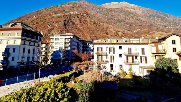 A residential area with multi-story buildings, a mountain in the background, and a clear sky. - Bernina Station Suite: 30 Steps to the Red Train (Tirano)