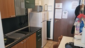 A compact kitchen with a microwave, refrigerator, sink, and a small dining area with a chair and table. - Bernina Station Suite: 30 Steps to the Red Train (Tirano)