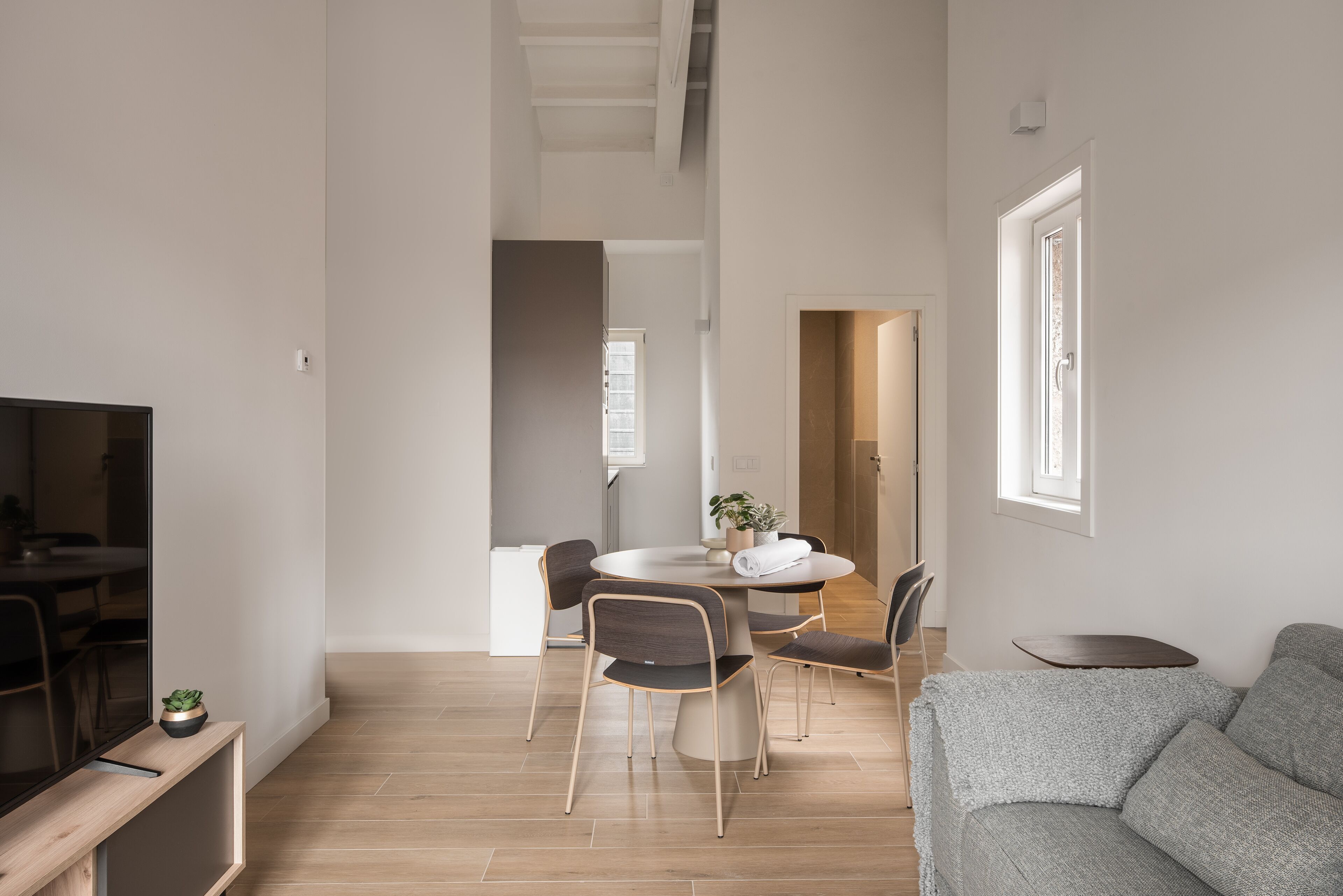 Un salon moderne avec un canapé gris, une table à manger et quatre chaises, ainsi qu’un téléviseur posé sur un meuble en bois.