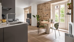Una cuina moderna amb una paret de pedra, una zona de menjador amb una taula rodona i cadires, i una finestra gran amb vista a vegetació.